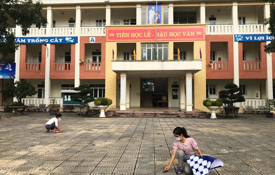 Giáo viên Trường Trung học cơ sở Trưng Vương (huyện Mê Linh) đánh dấu chỗ đứng cho học sinh bảo đảm giãn cách khi trở lại trường học.